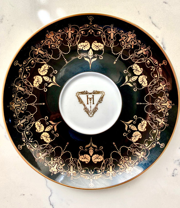 Top view of the Black and Gold Something Wicked Nouveau Saucer showcasing detailed gold floral patterns on a dark surface.